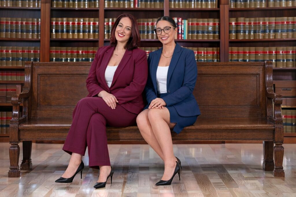 Austin DWI lawyers Angelica Cogliano and Deniz Kadirhan of CMK Defense, PLLC seated on a bench in front of law books