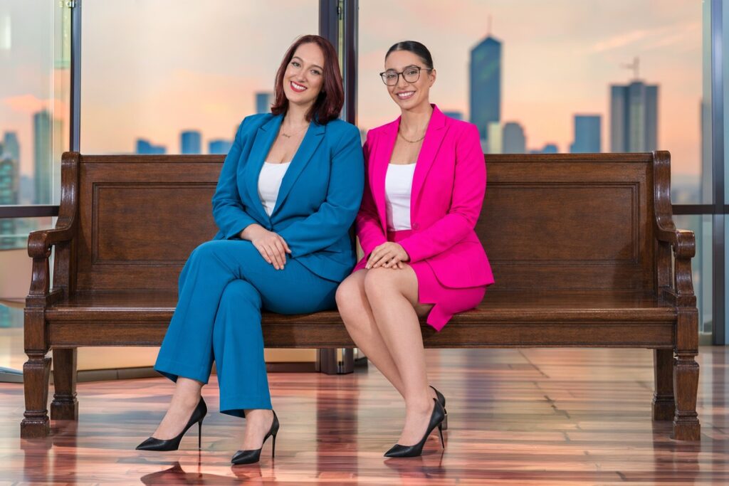 Austin theft lawyers Angelica Cogliano and Deniz Kadirhan of CMK Defense, PLLC seated on a bench in front of a city skyline